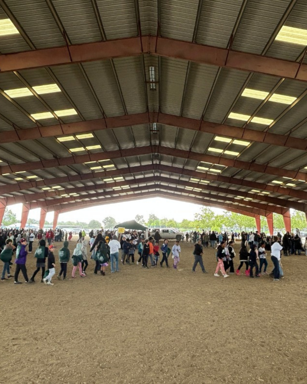 A large group of people congregates indoors under a spacious structure, engaging in activities or walking around.