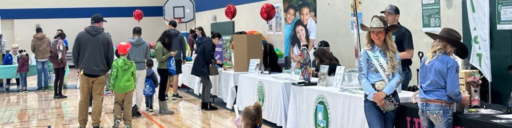 A community event with booths, attendees milling about, and people engaging with activities, including a cowgirl in a hat.