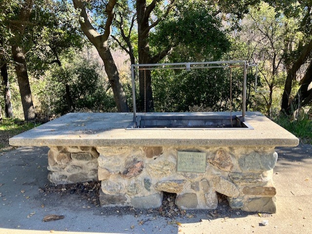 A stone outdoor barbecue grill in a wooded area.