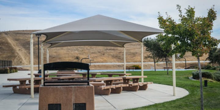 Outdoor picnic area with tables, grill, canopy, and trees.