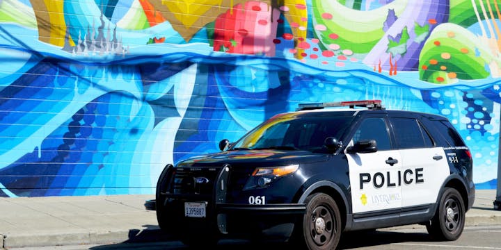 A police SUV parked in front of a vibrant mural featuring colorful waves and abstract designs.