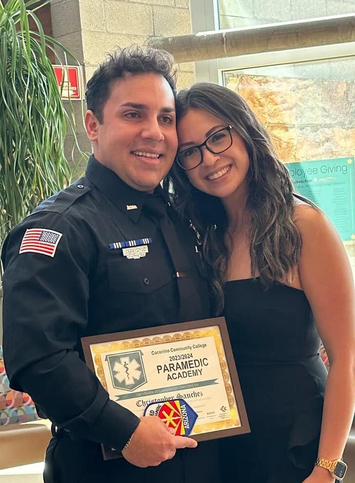 A person in a police uniform holds a certificate from a Paramedic Academy, standing next to a woman smiling.