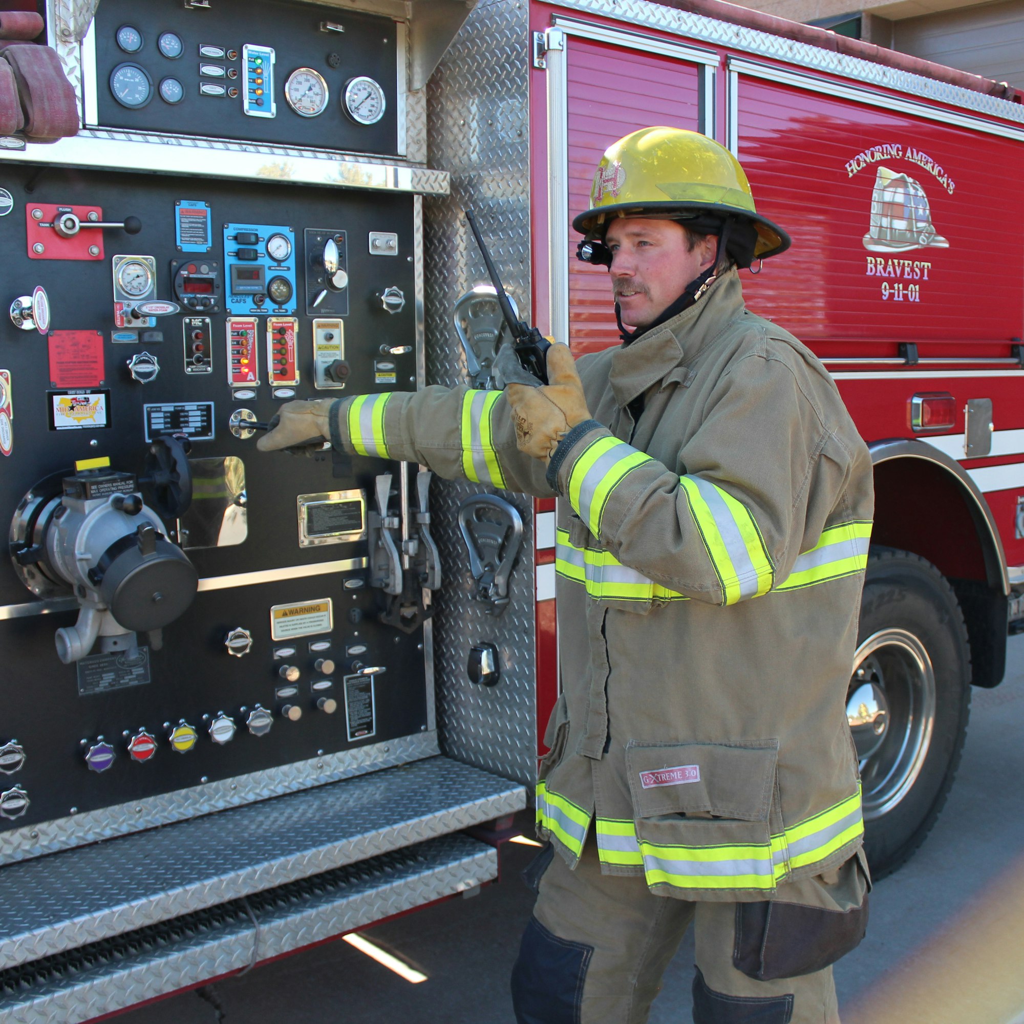 A firefighter in gear operates a fire truck control panel, communicating via radio.