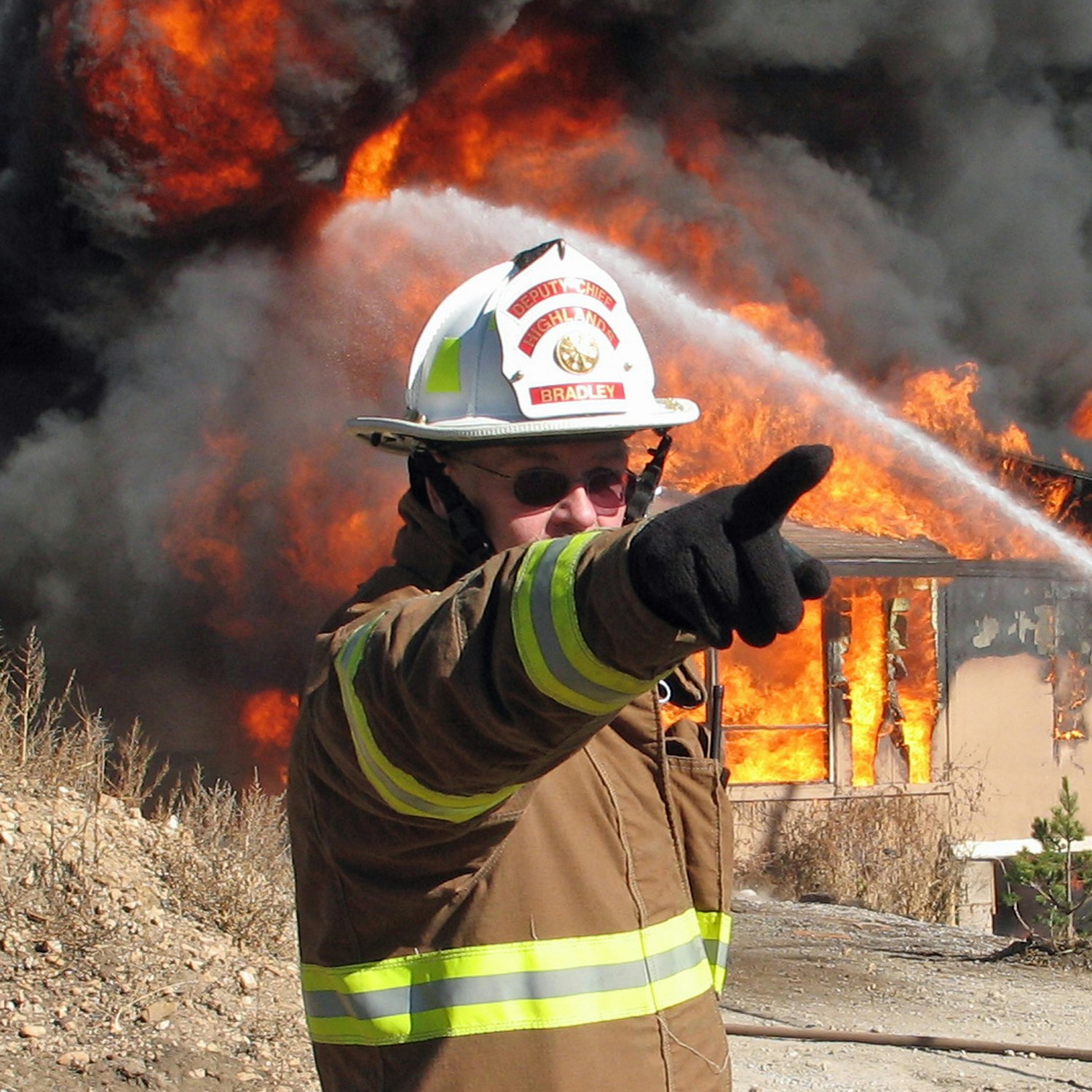 A firefighter gestures in front of a blazing fire.