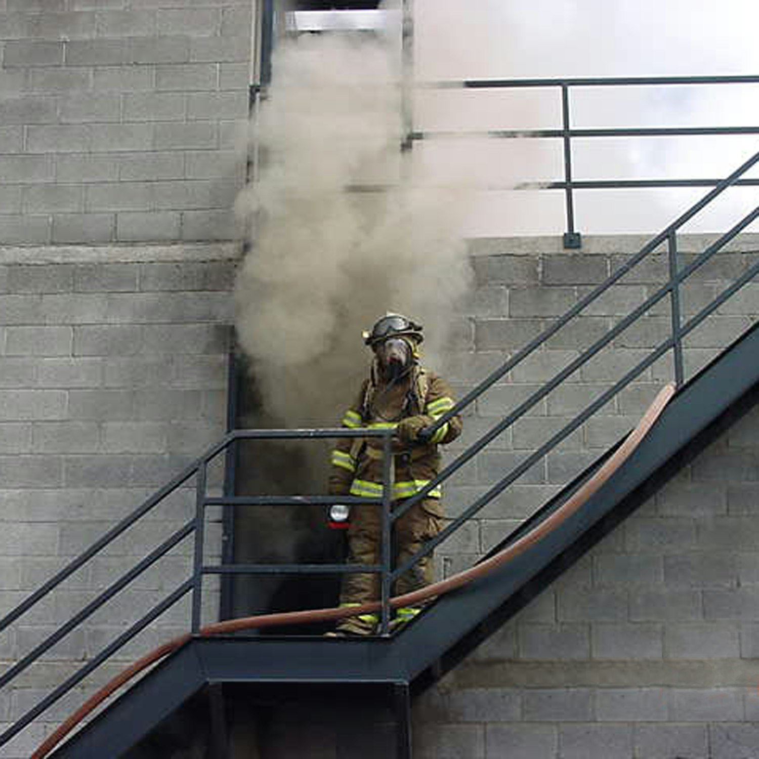 Firefighter on stairs with smoke, wearing protective gear and holding a hose.