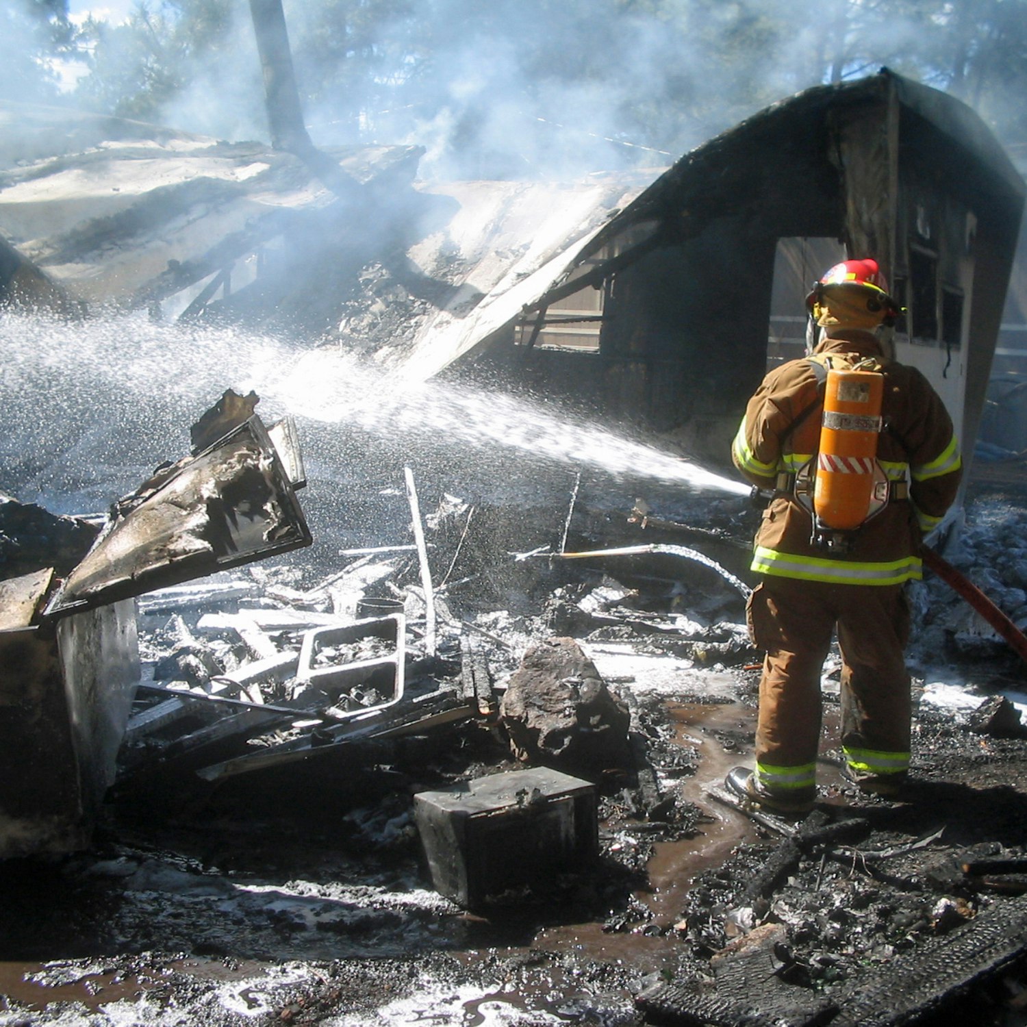 Firefighter extinguishing a smoldering house ruin.