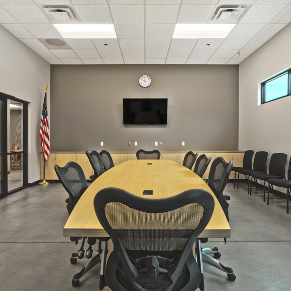 Conference room with a long table, chairs, an American flag, a TV, and a clock on the wall.