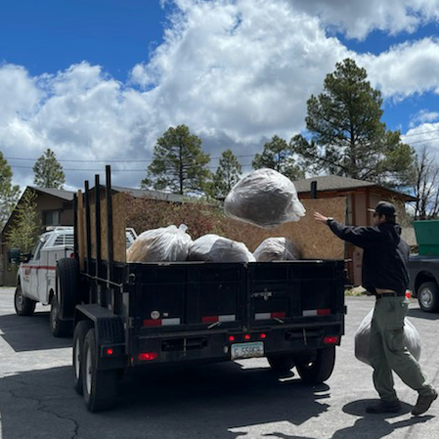 Person loading plastic-wrapped material onto a trailer under a sunny sky with clouds.