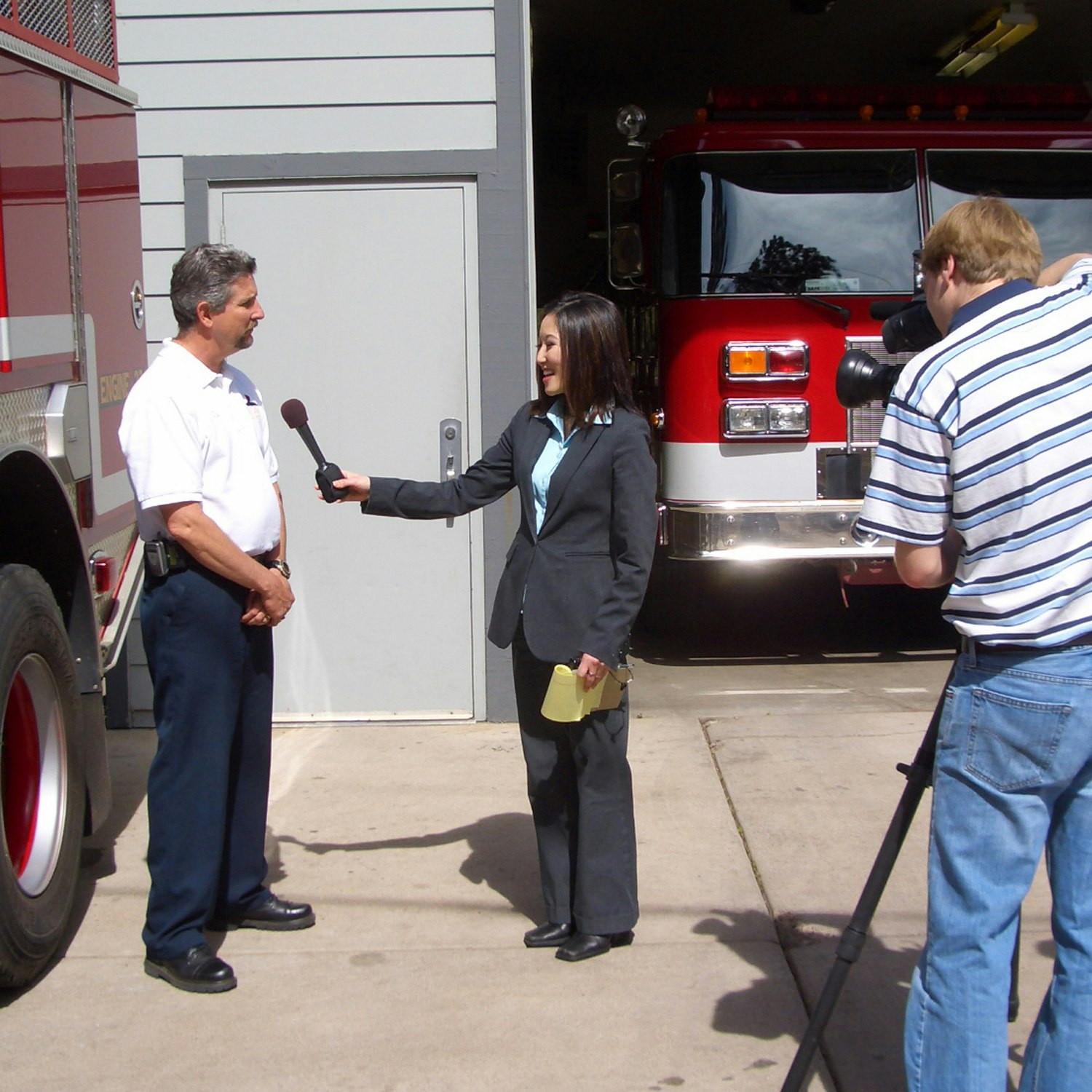 A reporter interviewing a man with a cameraperson filming near a fire truck.