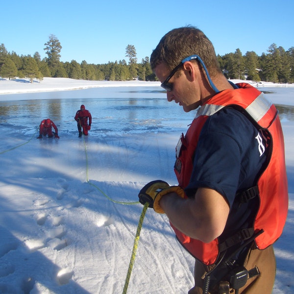 Ice rescue training with three individuals wearing safety gear on a frozen lake.