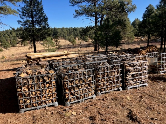Metal crates filled with chopped firewood in a forest clearing.