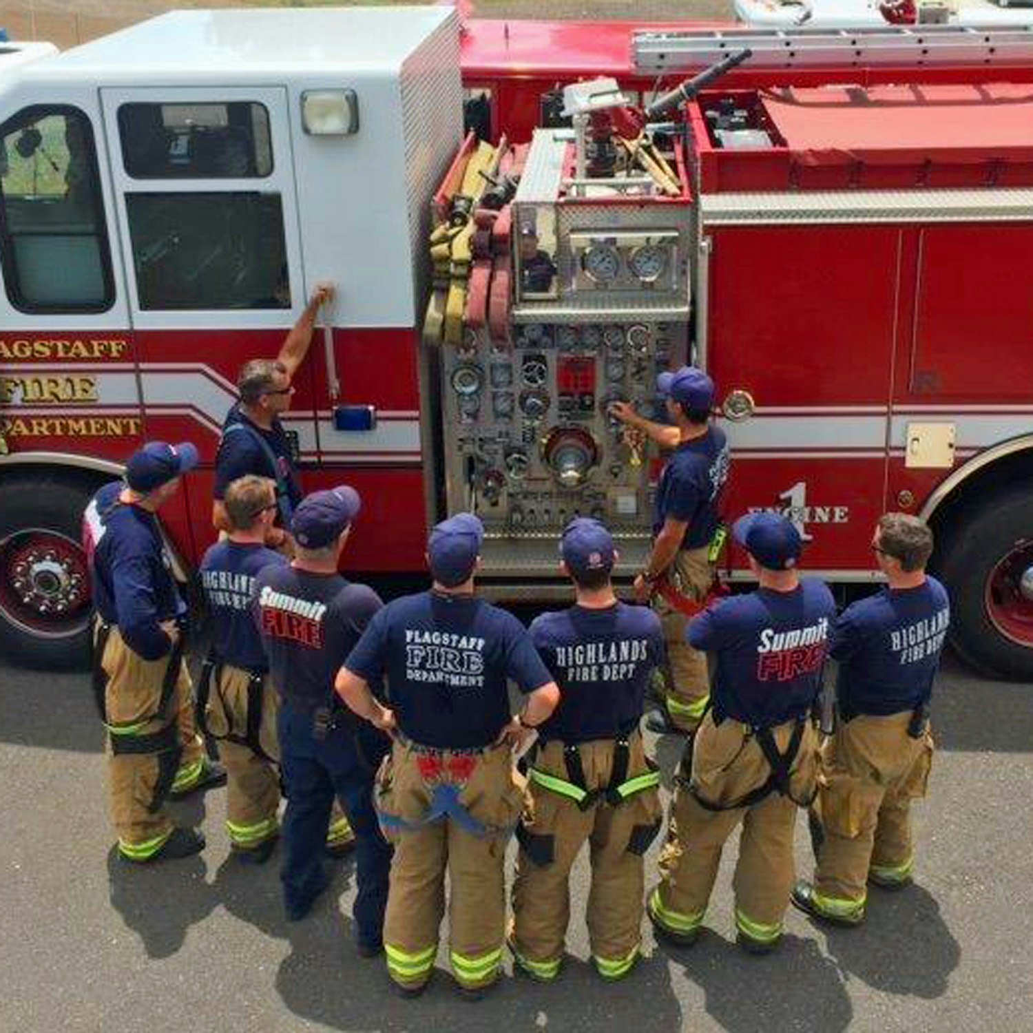 Firefighters in gear receiving training or instruction beside a fire truck.