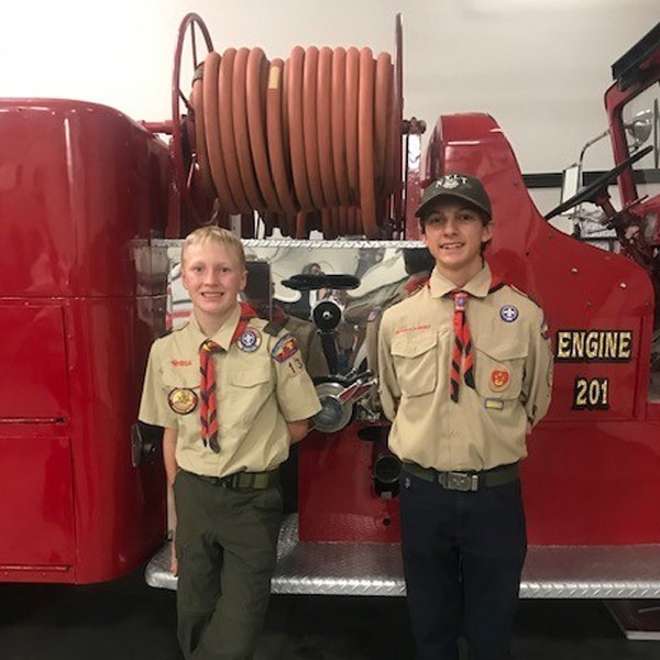 Two scouts in front of a vintage red fire engine.