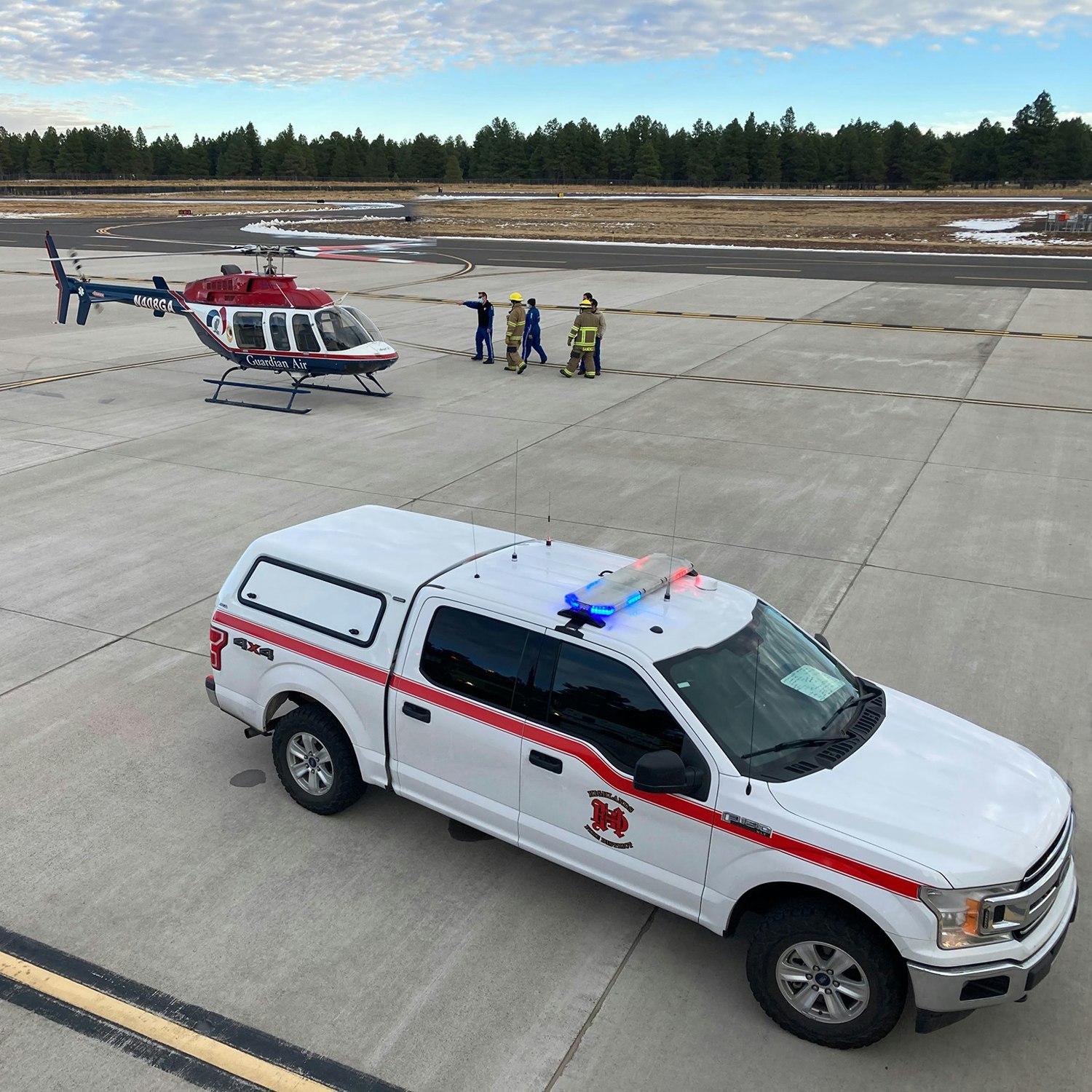 Emergency services with a helicopter, vehicle, and personnel at a helipad.