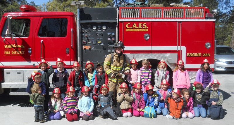 A group of children with a firefighter in front of a fire truck.