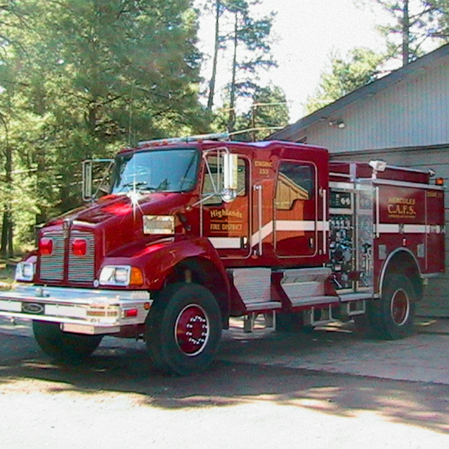 A red fire truck parked outdoors with trees in the background.