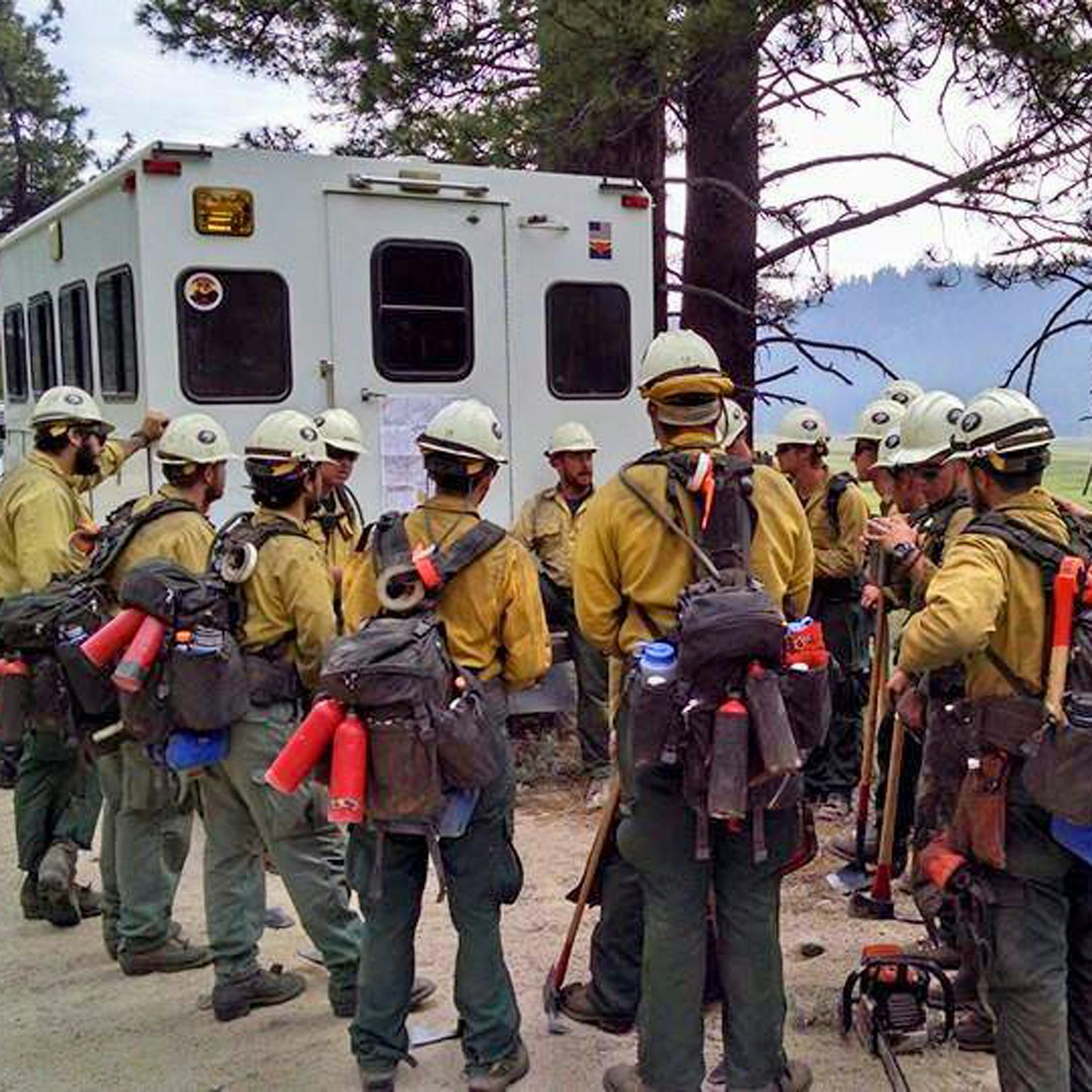 A group of firefighters in protective gear gathered in front of a vehicle, possibly preparing for a mission.