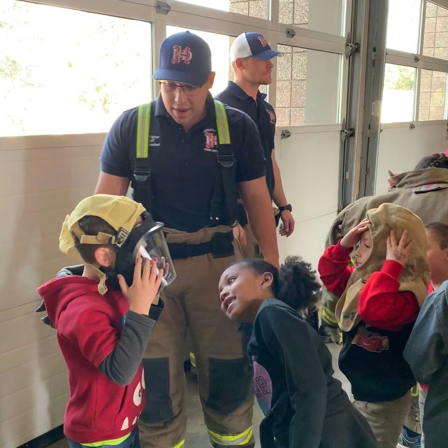 Firefighters interacting with kids, one wearing a fire helmet.