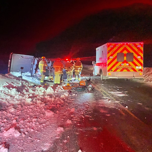 Firefighters at a nighttime roadside emergency with an overturned vehicle and an ambulance present.