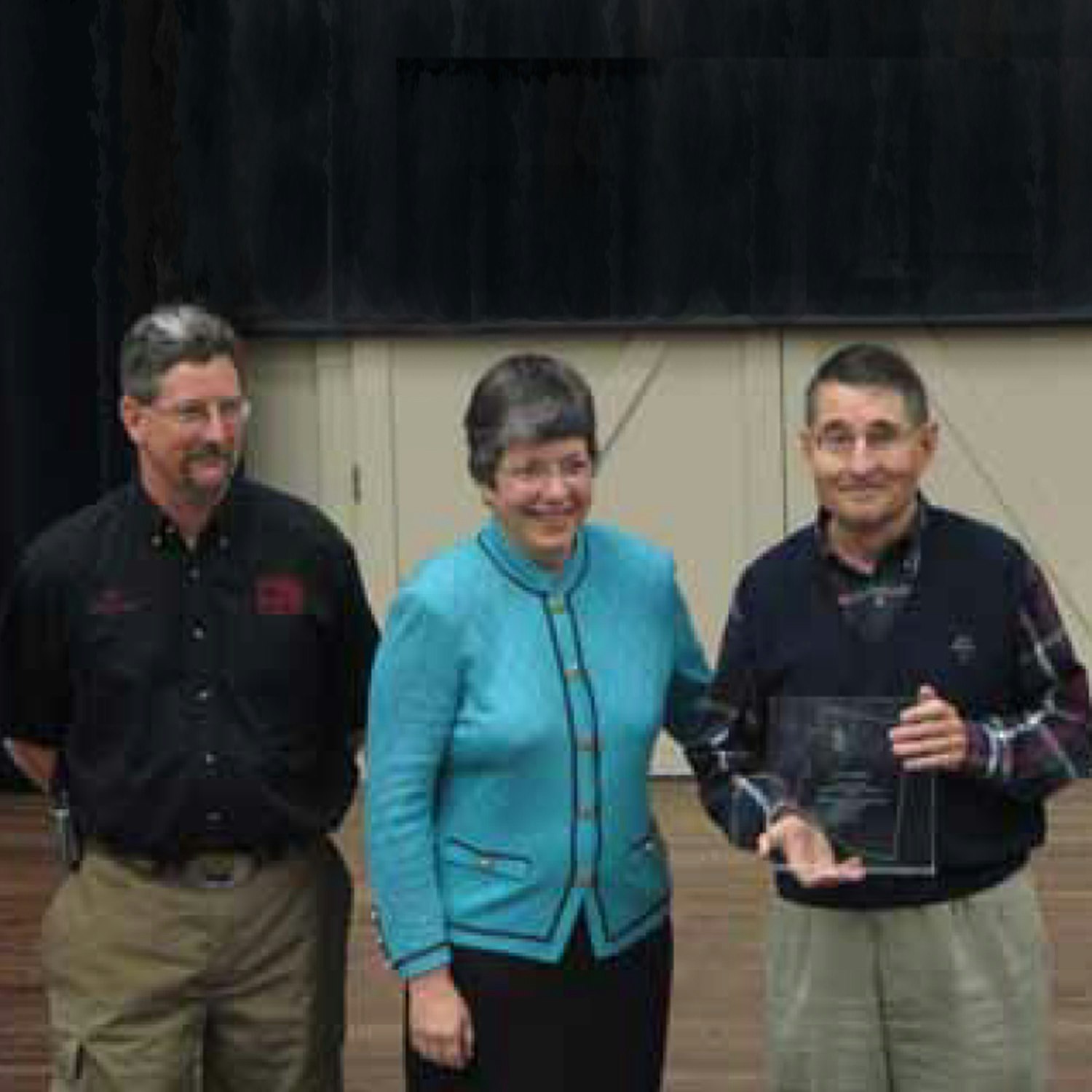 Three people posing, one holding an award.