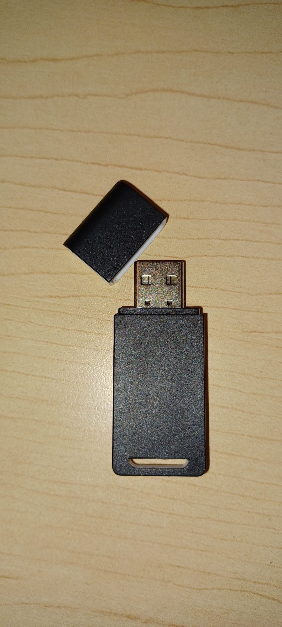 A black USB flash drive with its cap removed, on a wood surface.