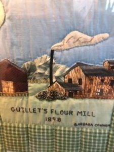 Quilt art depicting Guillet's Flour Mill with buildings, smoke, and mountains, labeled "1898" and "Barbara Chapman."