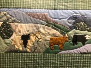 Quilted scene with cows and hills, featuring earthy tones and green plaid border.
