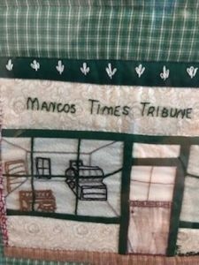 Quilt panel with "Mancos Times Tribune" text and a window scene, featuring shelves and decor.