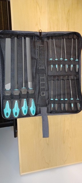 A toolset with various files and screwdrivers in a black case with turquoise handles on a wooden surface.