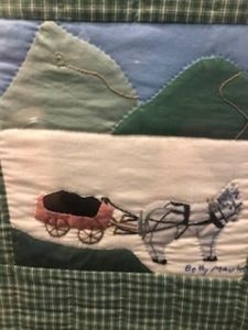 Quilt art depicting a horse pulling a red cart in a mountainous landscape.