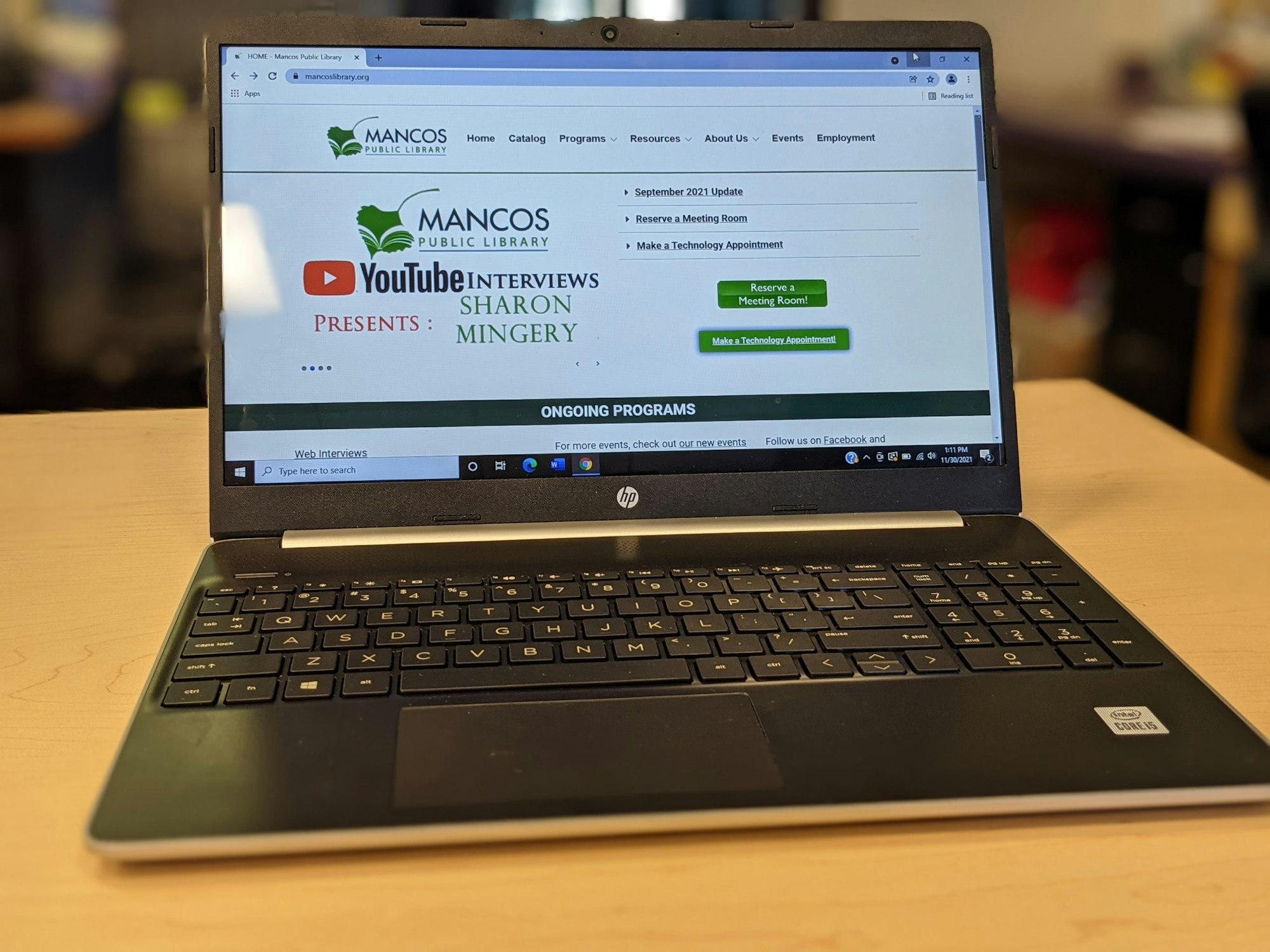 A laptop displaying a webpage for Mancos Public Library featuring a YouTube interview presentation.