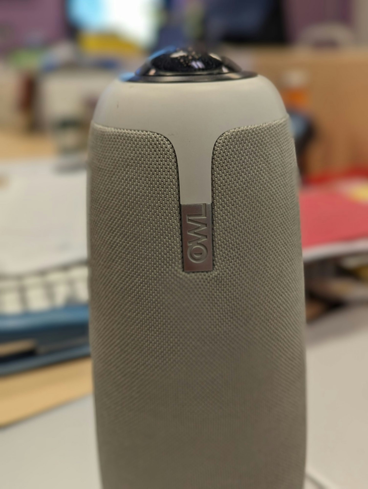 A gray, fabric-textured smart speaker or device on a table with a blurred background.