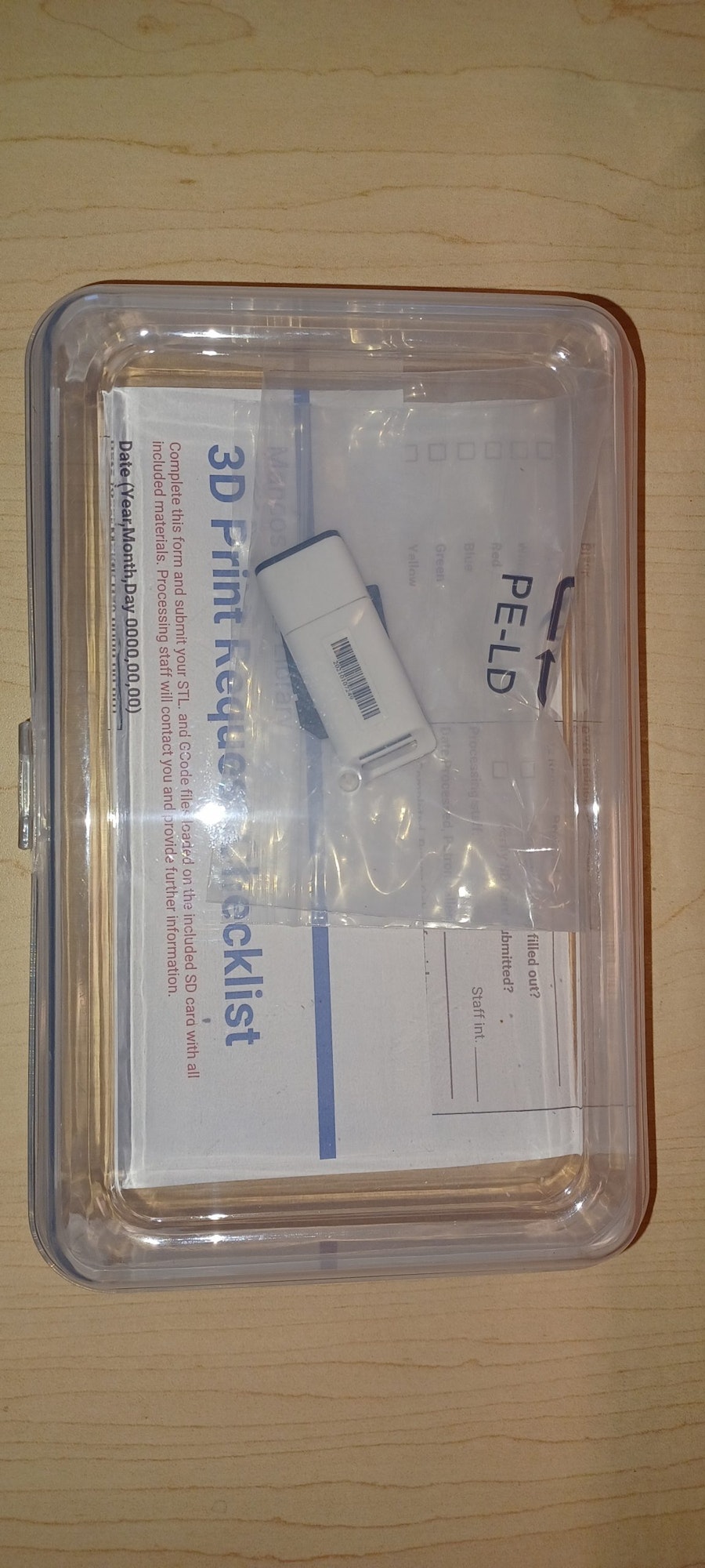 A clear plastic container with a 3D print request form and a USB drive inside.