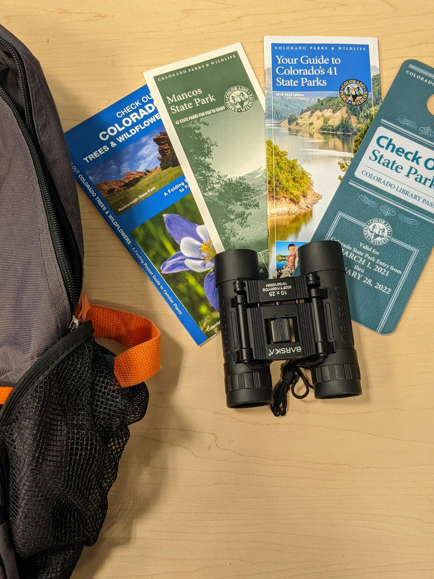 Backpack, binoculars, and brochures for Colorado state parks on a table.