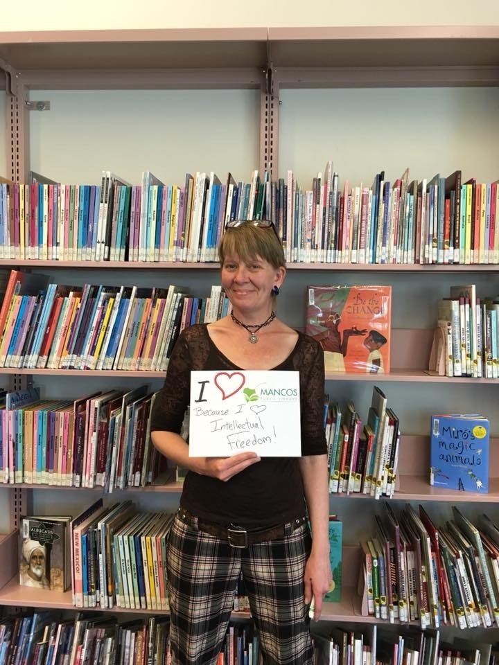 A person holding a sign supporting intellectual freedom stands in front of bookshelves in a library.