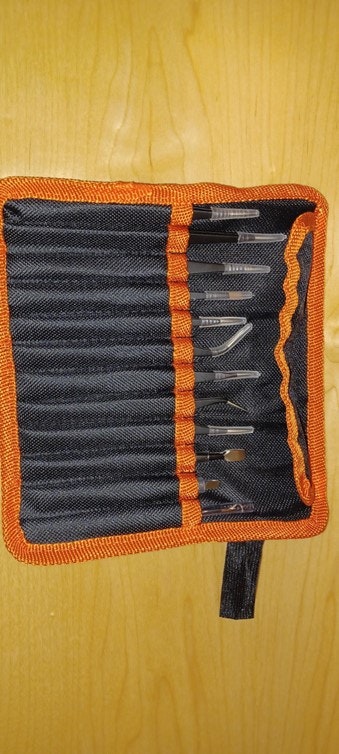A black and orange tool pouch containing various metal tools on a wooden surface.