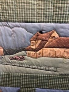 A quilted pattern depicting a house with a chimney, surrounded by textured fabric resembling clouds and greenery.