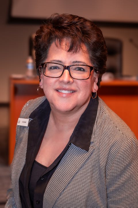 A person smiling in formal attire, wearing glasses and a name tag.