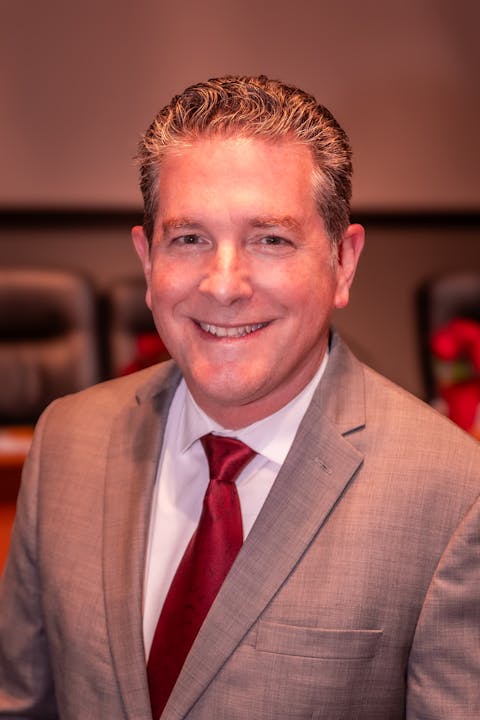 A man in a suit and red tie smiling.