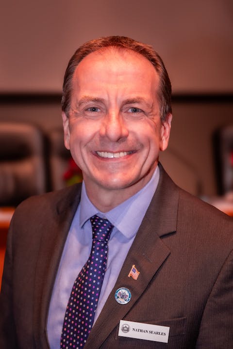 A smiling man in a suit with a flag pin, name tag, and tie.
