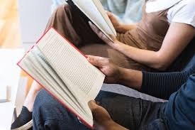 People reading books, sitting closely together.