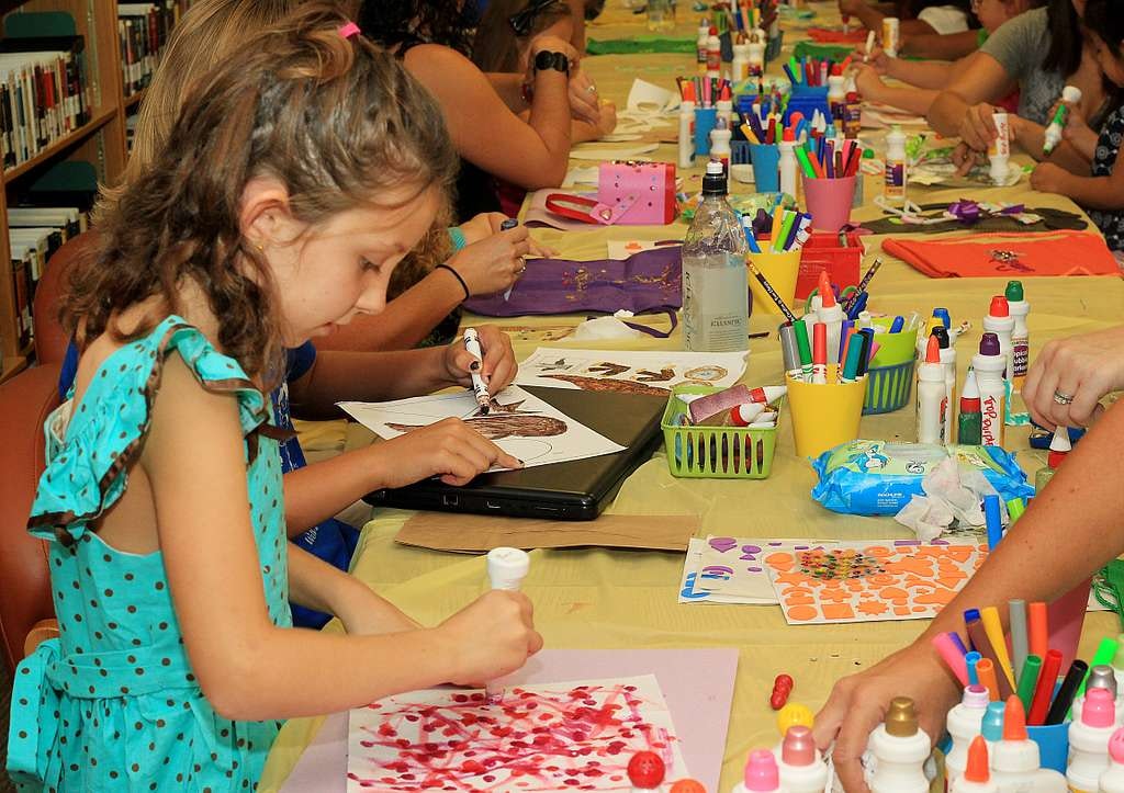 Children crafting at a table with art supplies, using markers and paper.
