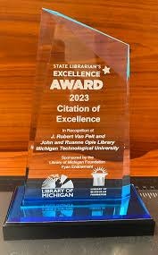A transparent award trophy with text, atop a black base with a logo, dated 2023.