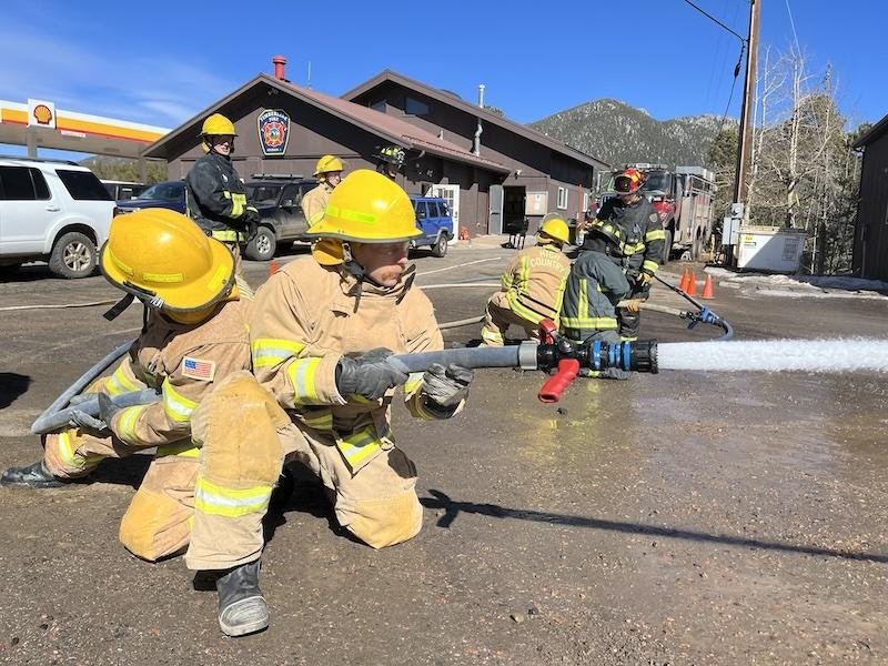 Firefighters in protective gear training with a hose, spraying water.
