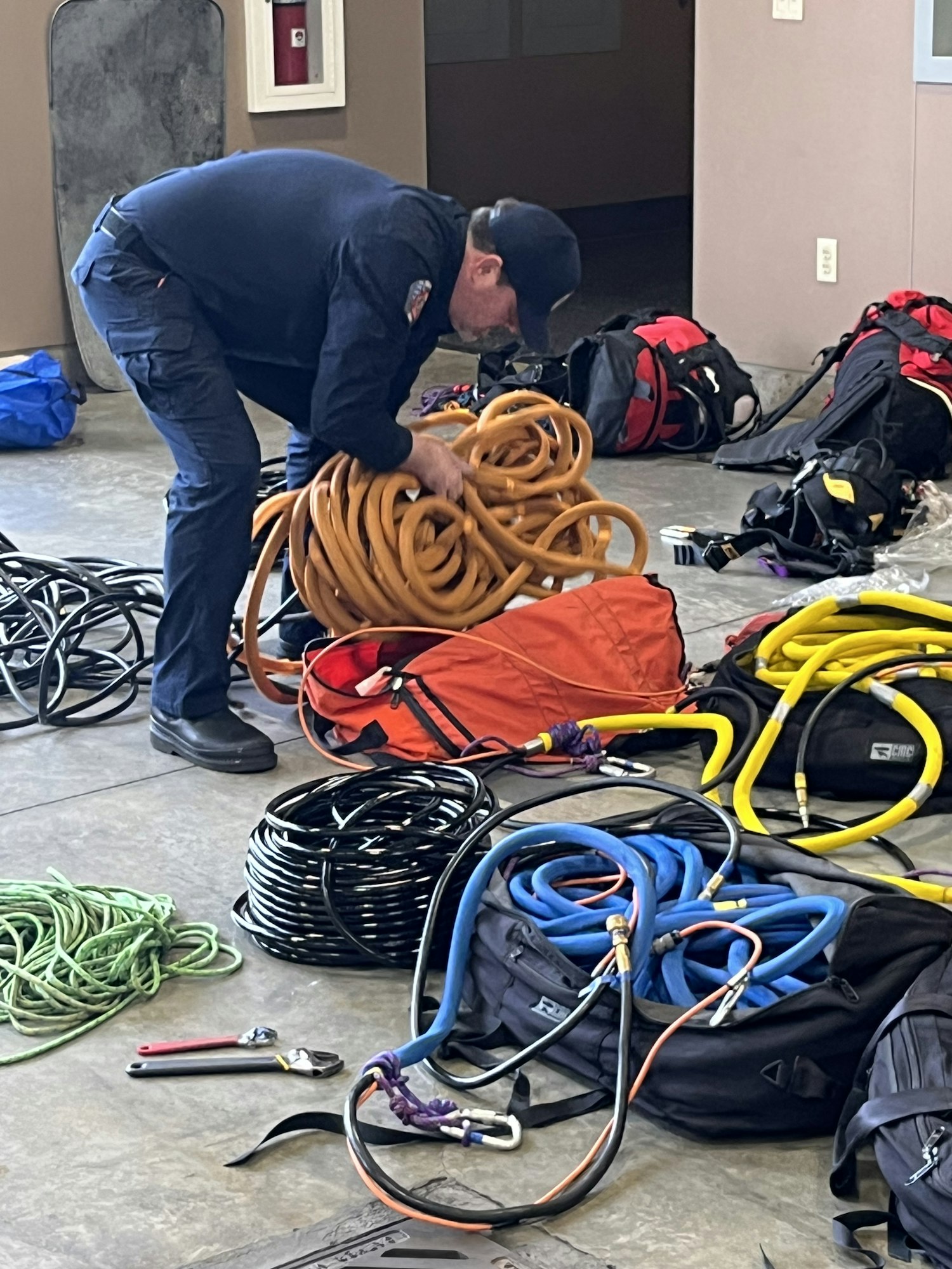 A person organizes various ropes and equipment, including bags and tools, likely for rescue or emergency services.