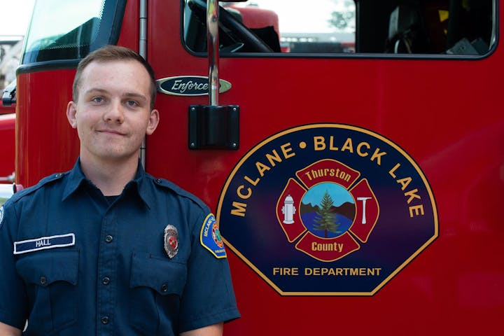Firefighter in uniform stands next to a McLane-Black Lake Fire Department truck with a visible logo.