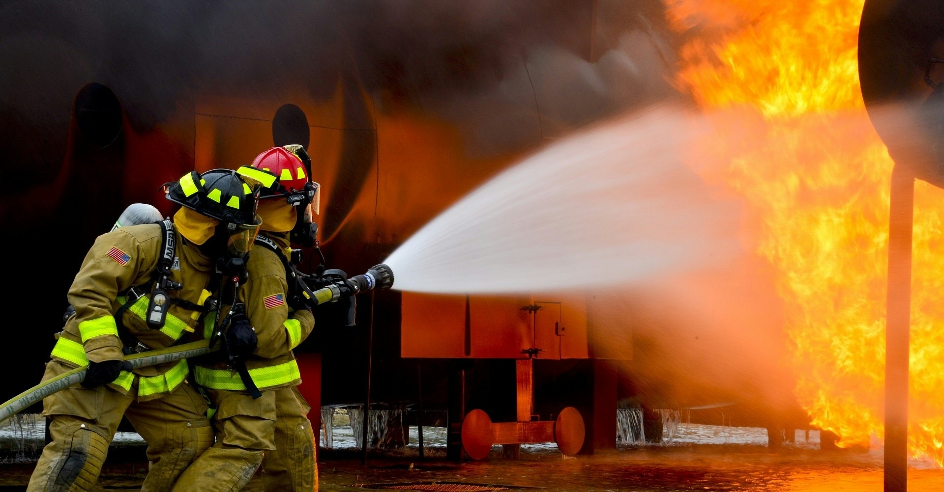 Firefighters battle a blaze, using a hose to spray water at a large fire, showcasing teamwork and bravery in action.