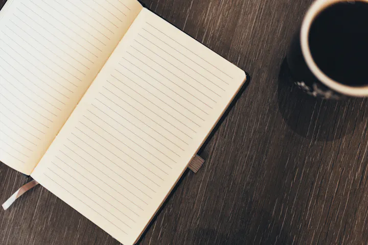 An open lined notebook next to a cup of coffee on a wooden table. Perfect for jotting down thoughts or notes.