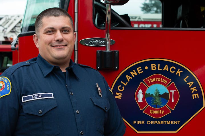A firefighter in uniform stands next to a McLane-Black Lake Fire Department vehicle.