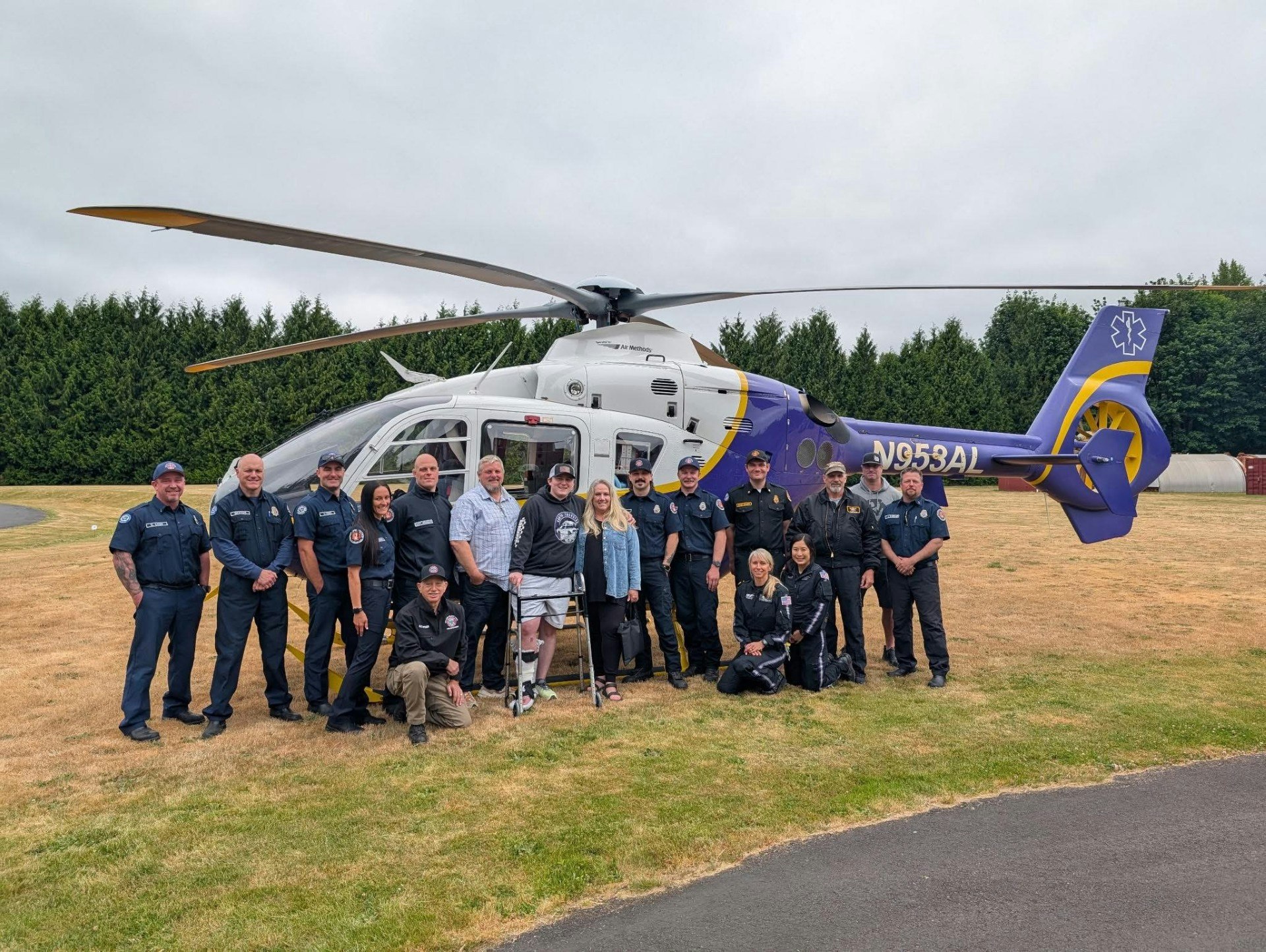 A group of emergency responders poses for a photo by a helicopter in a grassy area, showcasing teamwork and service.
